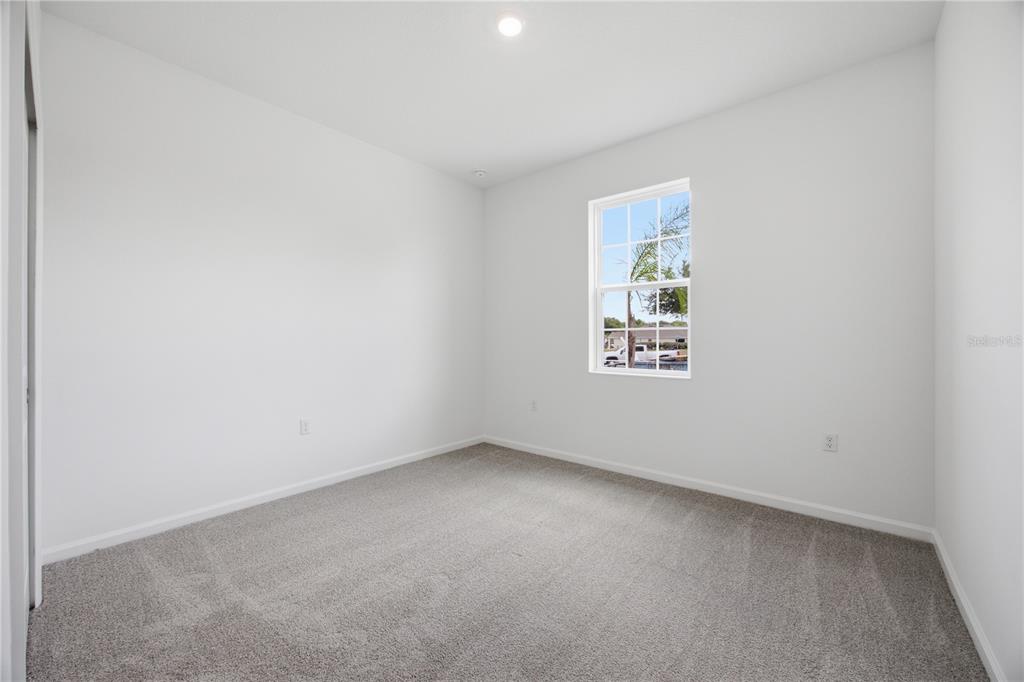 An empty bedroom features white walls, gray carpeting, and a single window — 6209 SANDERS GROVE CIRCLE, OKAHUMPKA, FL