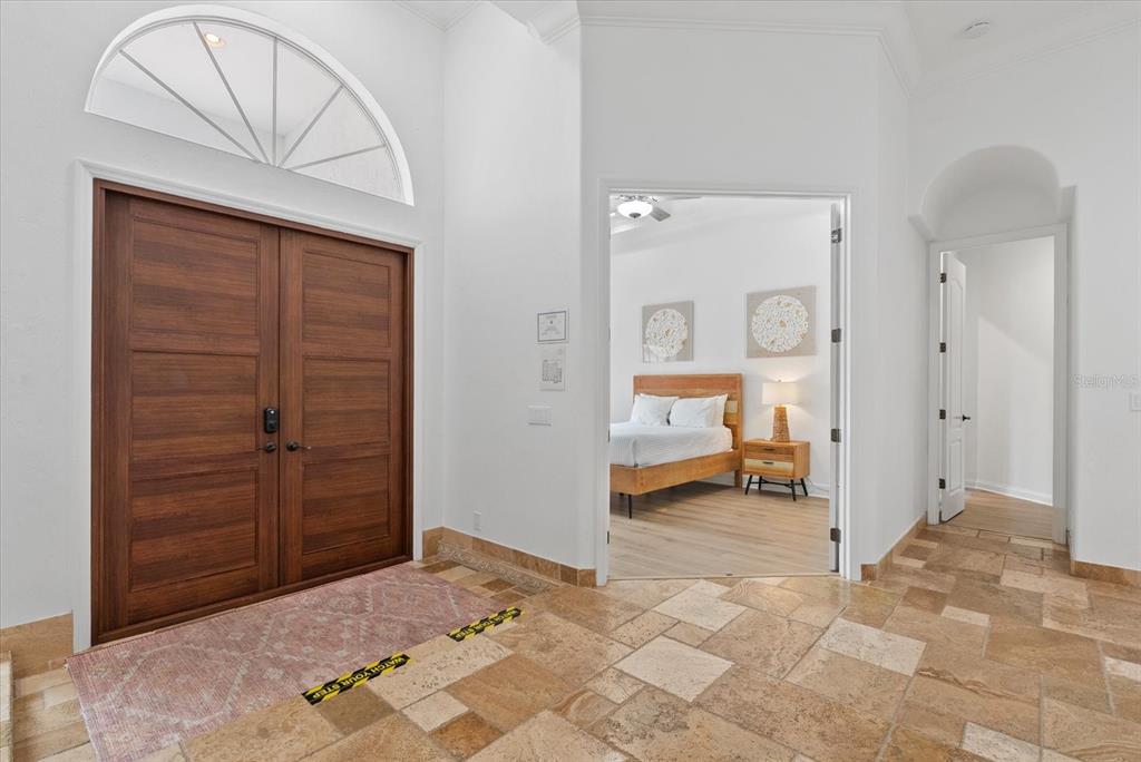 A foyer with a double wood door, stone tile flooring, and a view into a bedroom — 3508 LA PALOMA AVENUE, SARASOTA, FL