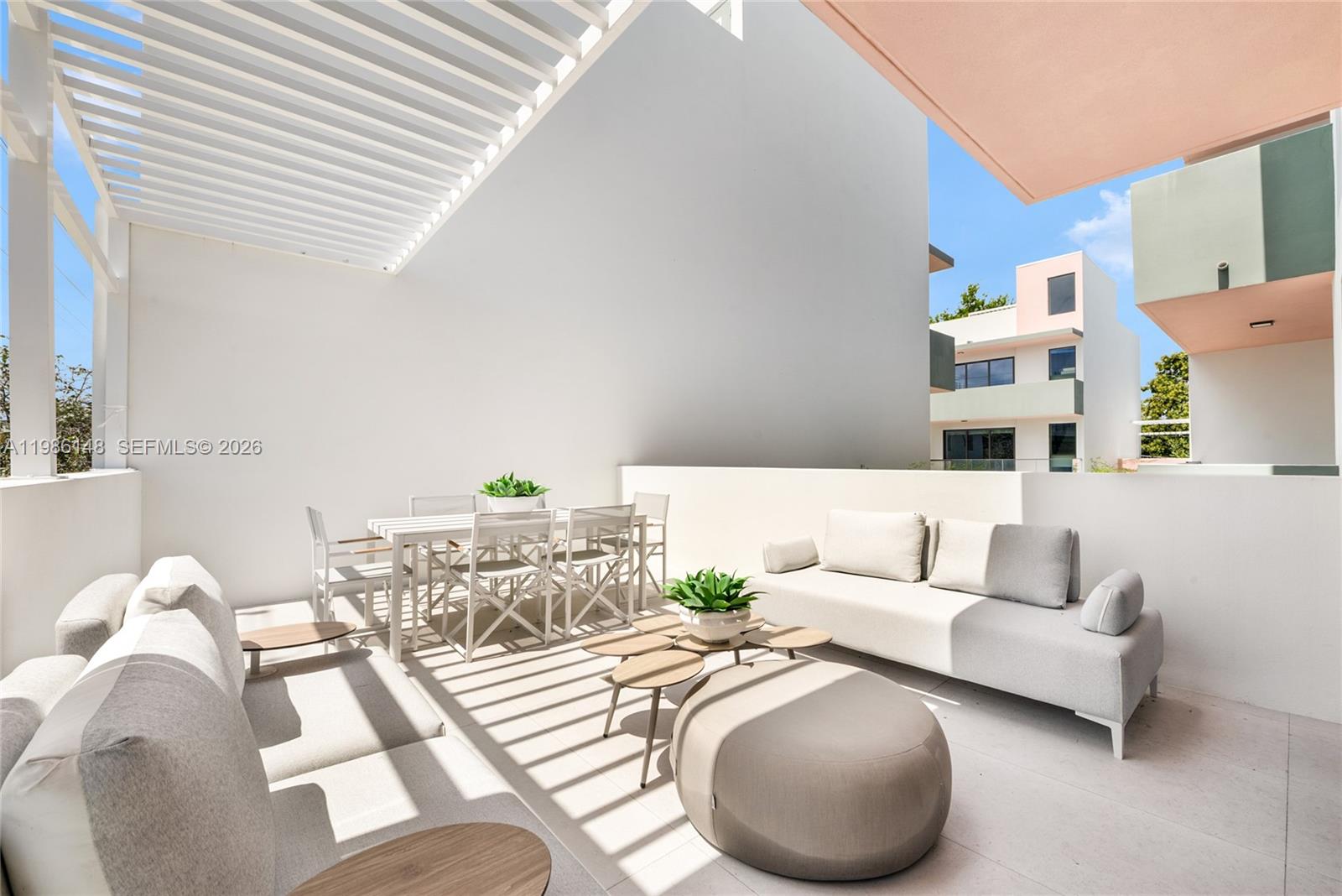 A modern outdoor patio features white walls, a slatted pergola, and contemporary lounge furniture — 721 SW 11th Street # A, Miami FL 33129, MIAMI, FL