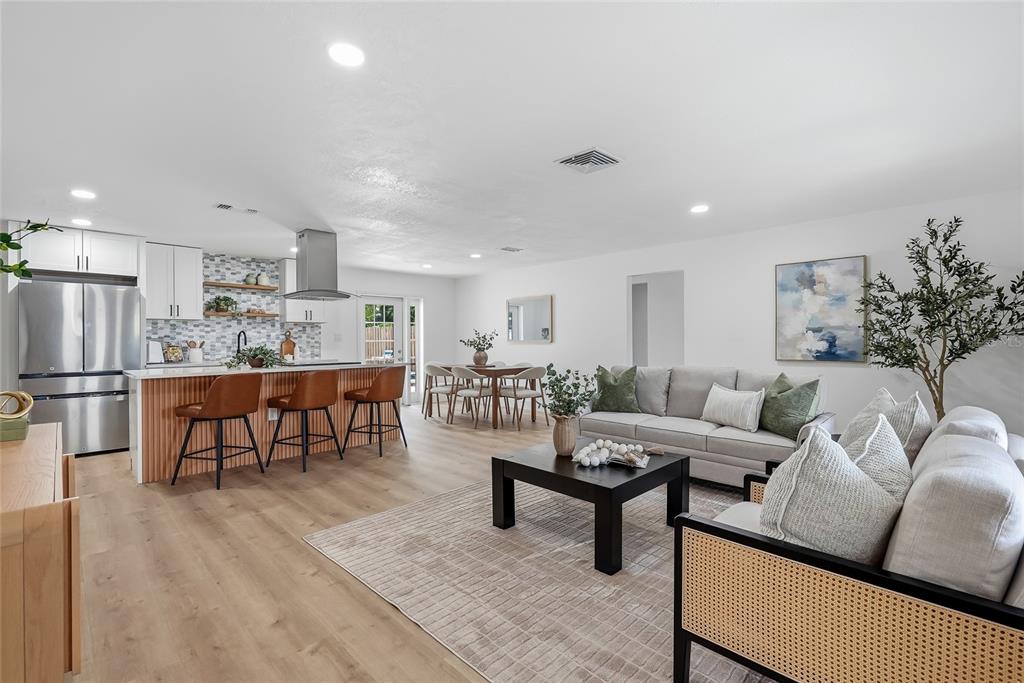 An open-concept living room and kitchen featuring light wood flooring and modern neutral furnishings — 6419 PELICAN DRIVE S, ST PETERSBURG, FL
