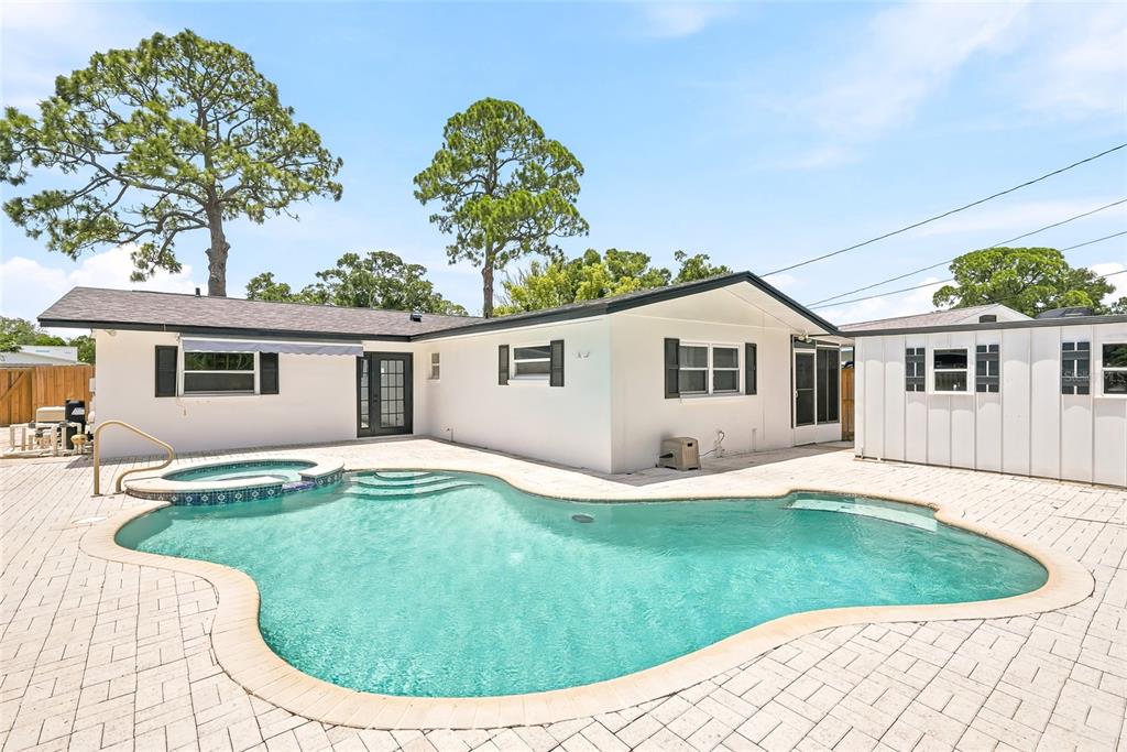 A white house with a swimming pool and spa sits on a paved patio — 6419 PELICAN DRIVE S, ST PETERSBURG, FL