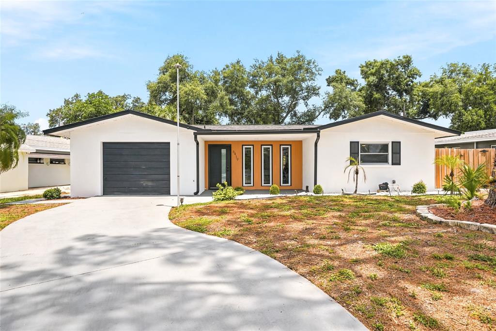 A single-story house with a white exterior, a dark garage door, and an orange entryway — 6419 PELICAN DRIVE S, ST PETERSBURG, FL