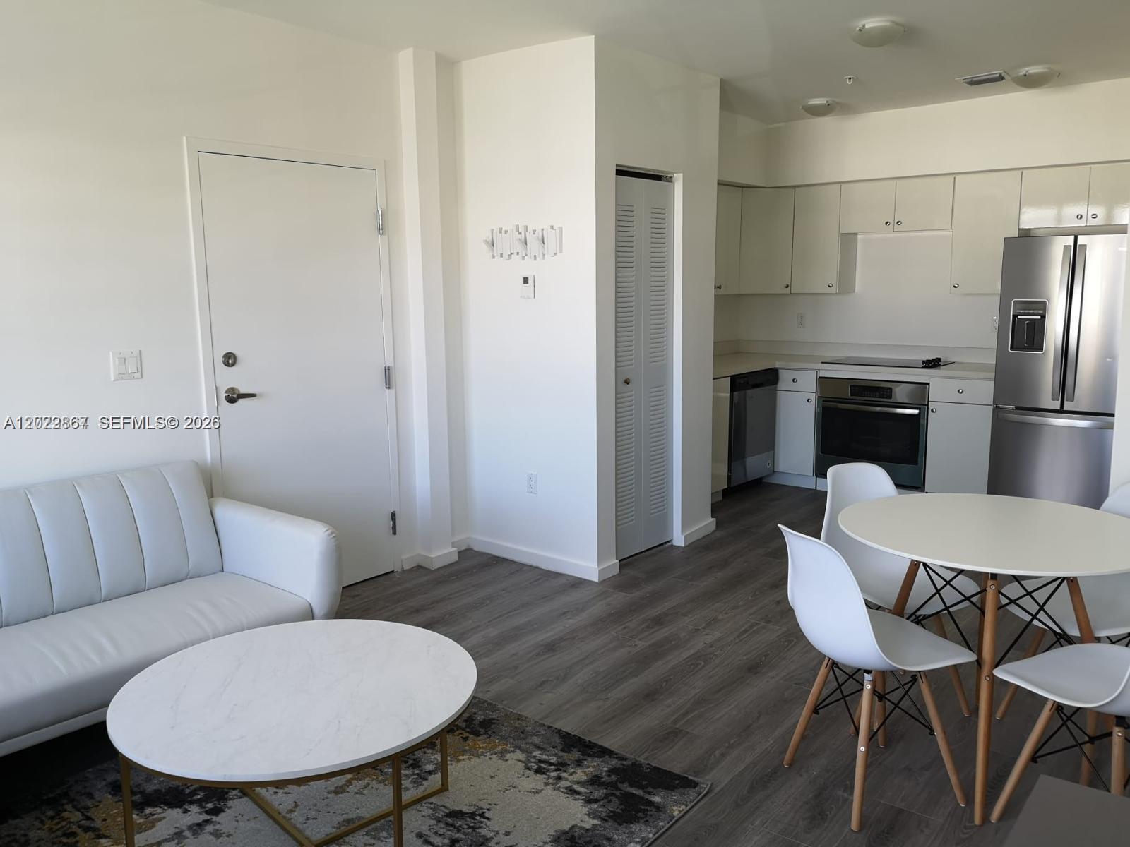 A living room and kitchen area feature white cabinetry, stainless steel appliances, and wood-look flooring — MIAMI BEACH, FL