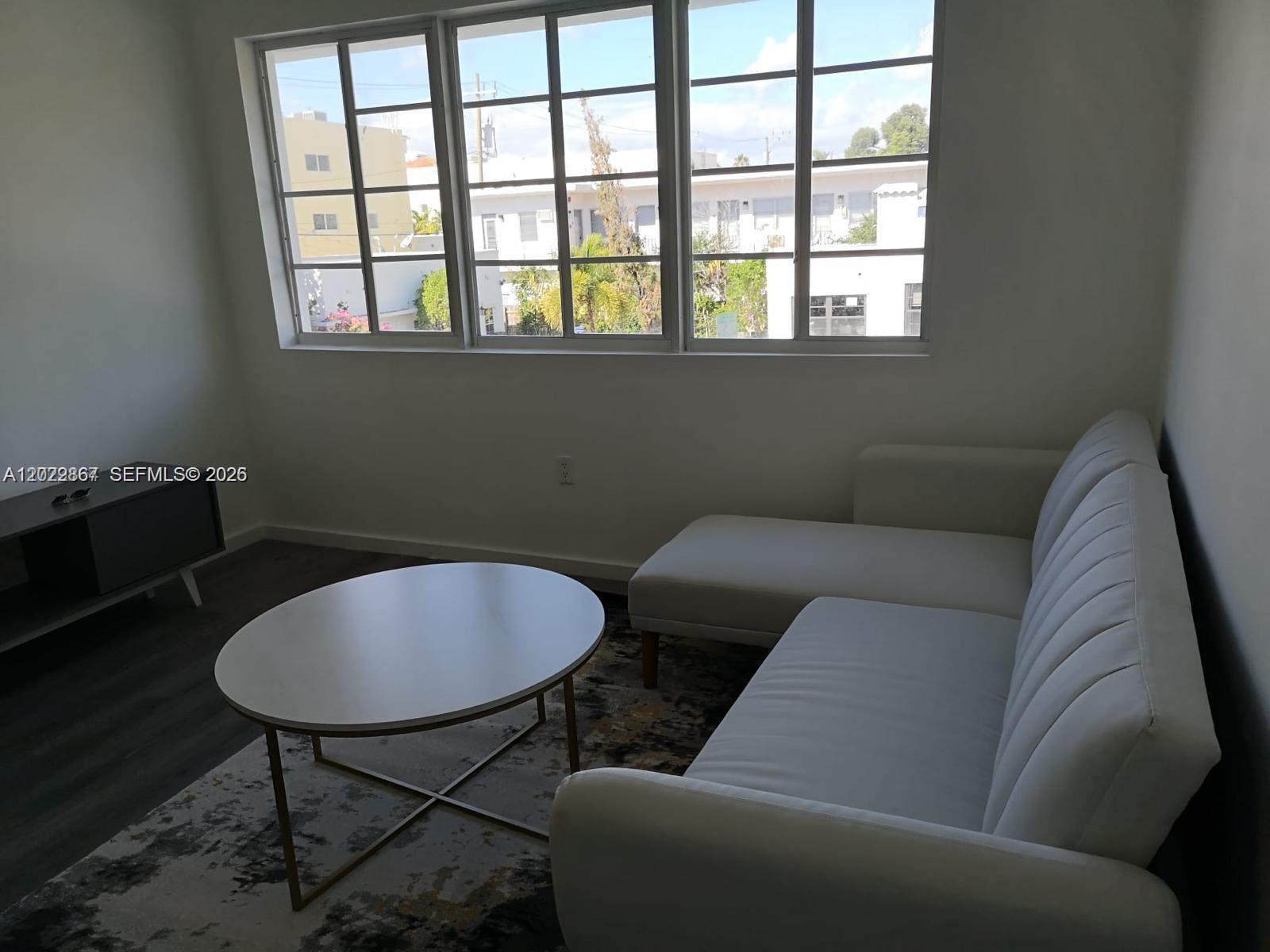 A living room features a white sectional sofa, a round coffee table, and large windows — MIAMI BEACH, FL