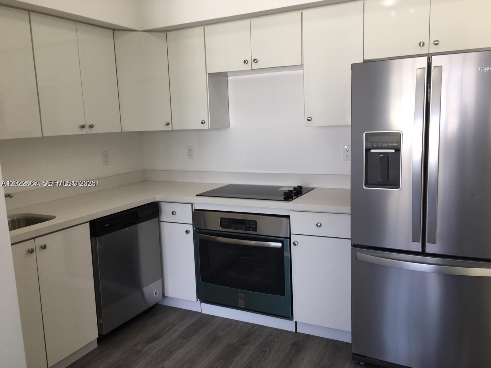 A kitchen features white cabinets, stainless steel appliances, and light countertops over wood-look flooring — MIAMI BEACH, FL