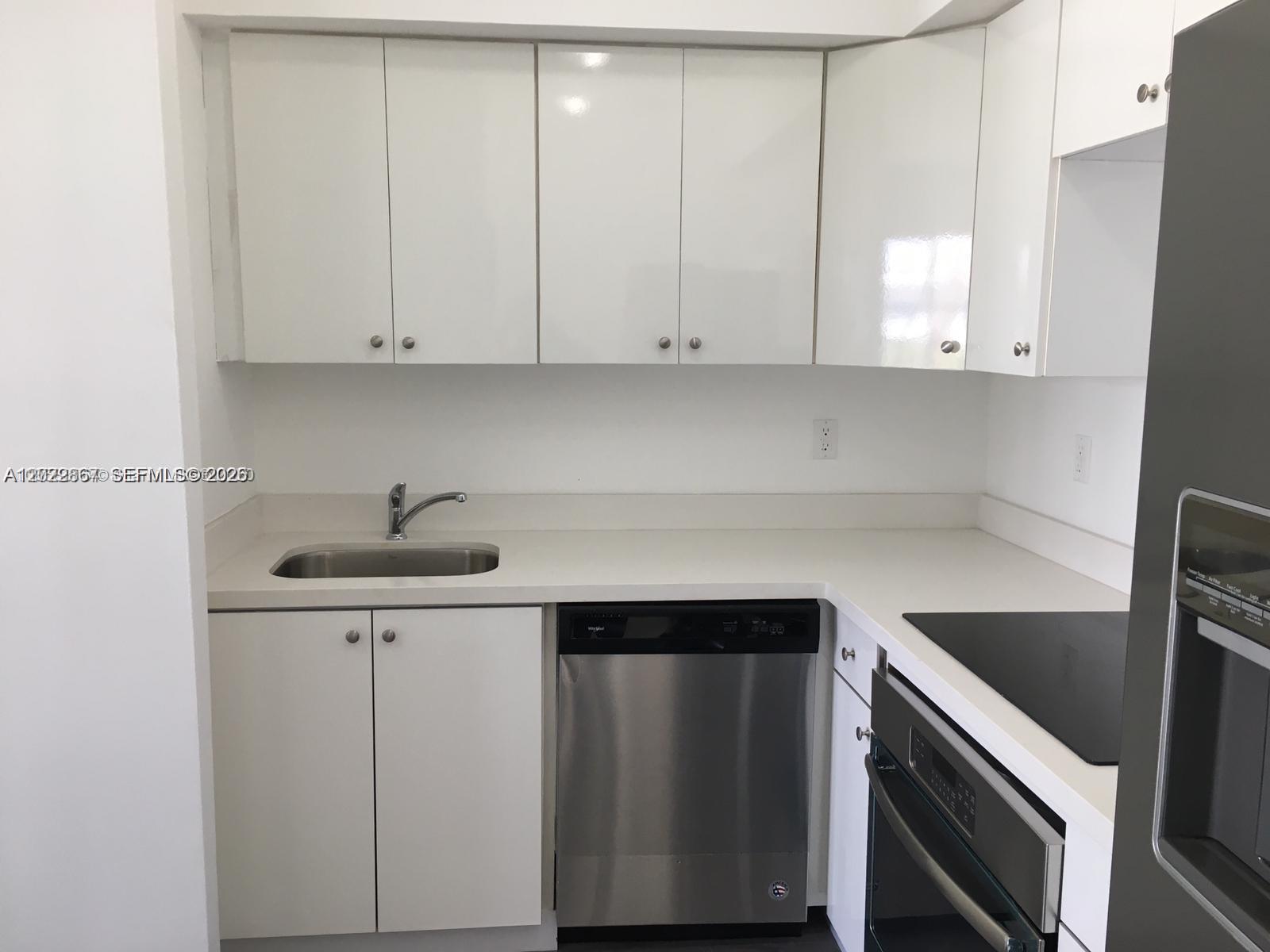A kitchen features white cabinets, a stainless steel dishwasher, and a white countertop — MIAMI BEACH, FL