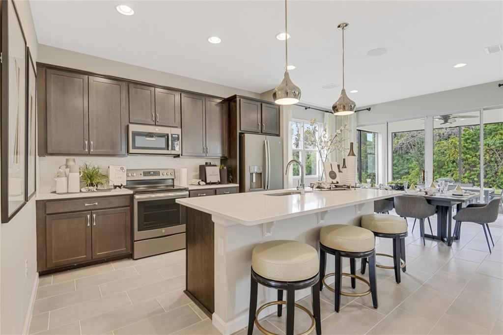 A modern kitchen features dark wood cabinetry, a large white island with stools, and tile flooring — 3451 MACCHI AVENUE, TAVARES, FL