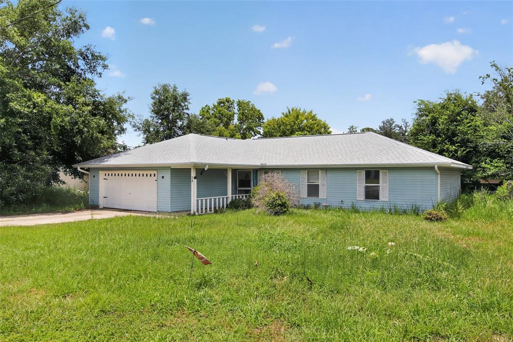A light blue, single-story ranch-style house with a garage and an overgrown front lawn — 28 PECAN RUN WAY, OCALA, FL