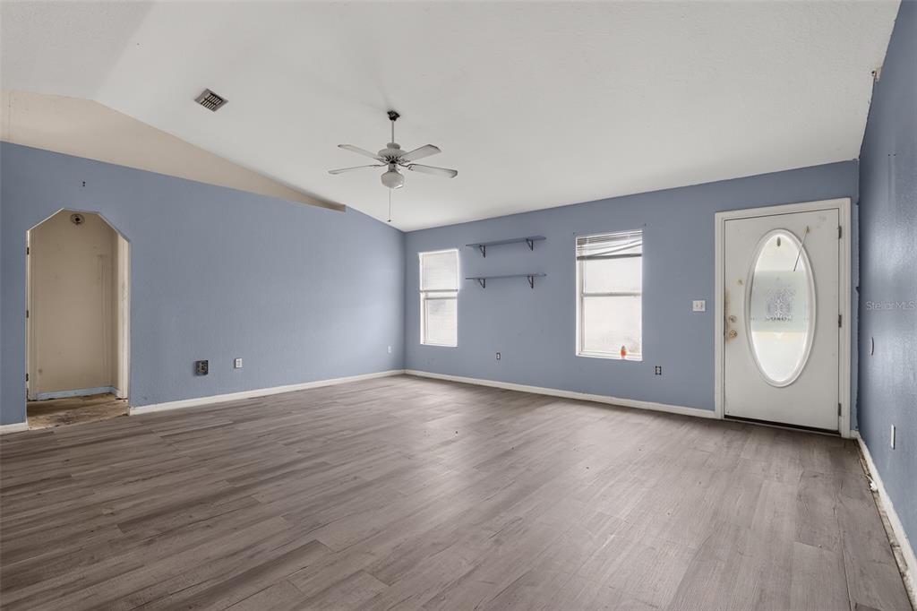 An empty room with blue walls, wood-look flooring, a ceiling fan, and a front door — 28 PECAN RUN WAY, OCALA, FL