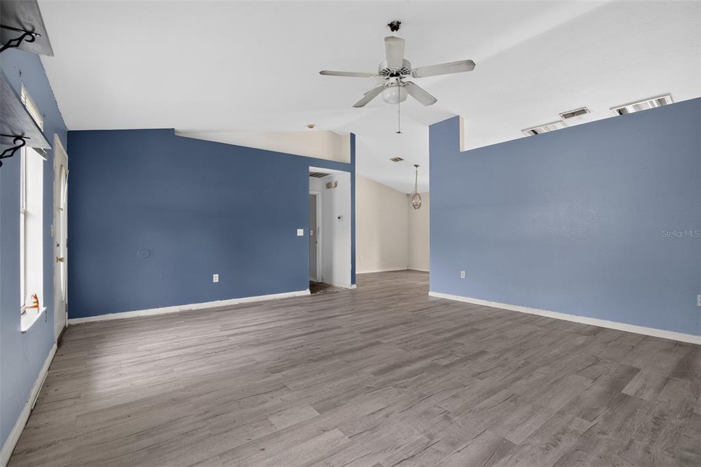 A living room with blue walls, light wood-look flooring, and a ceiling fan — 28 PECAN RUN WAY, OCALA, FL