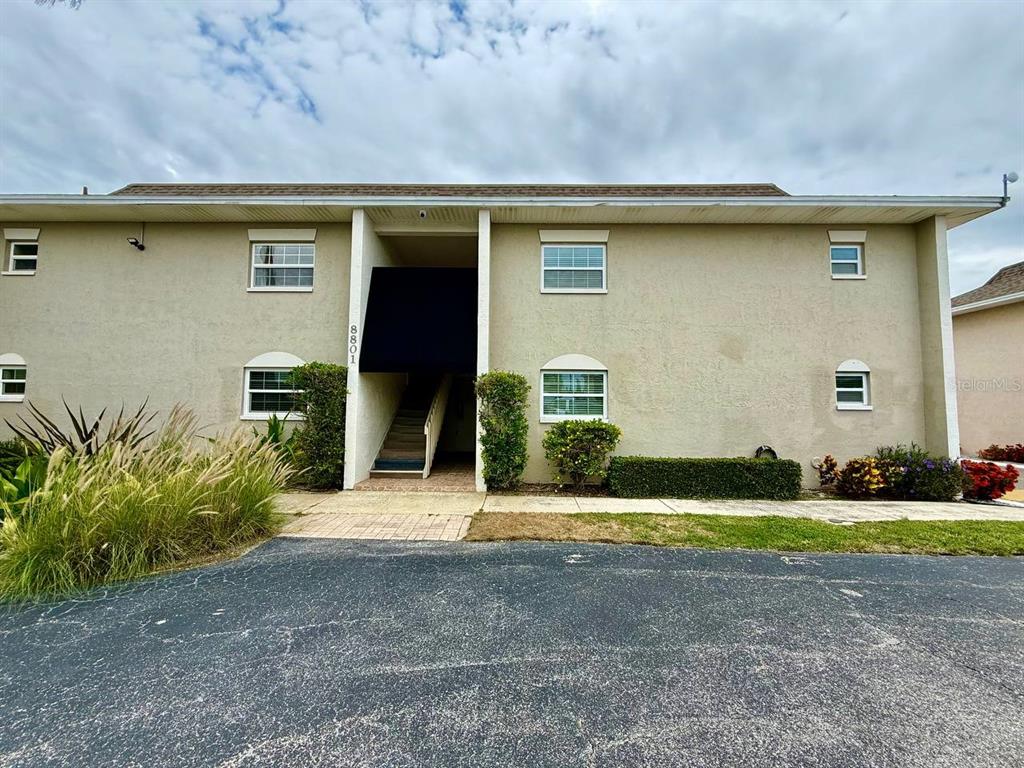 A two-story apartment building exterior features tan stucco walls and a central covered staircase — 8801 BAY POINTE DRIVE UNIT 102, TAMPA, FL