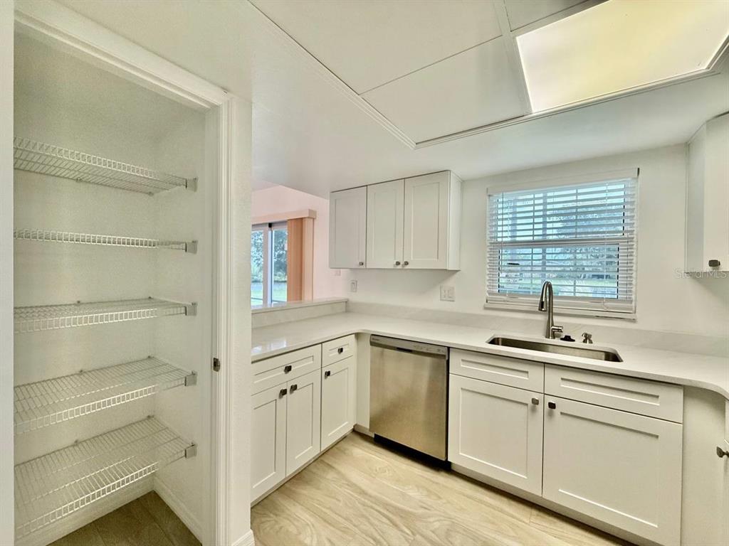 A kitchen features white cabinets, light countertops, a stainless steel dishwasher, and a walk-in pantry — 8801 BAY POINTE DRIVE UNIT 102, TAMPA, FL