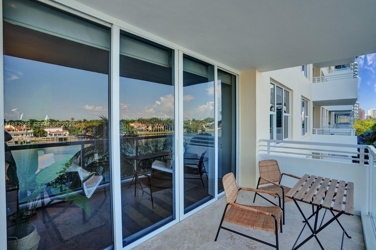 A balcony features a small wooden table, two wicker chairs, and sliding glass doors — 5600 Collins Ave # 5R, Miami Beach FL 33140, MIAMI BEACH, FL