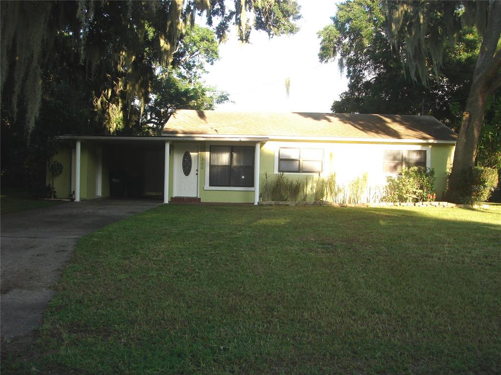 A single-story house with a carport, light green siding, and a large front lawn — 1300 PARK AVENUE, TAVARES, FL