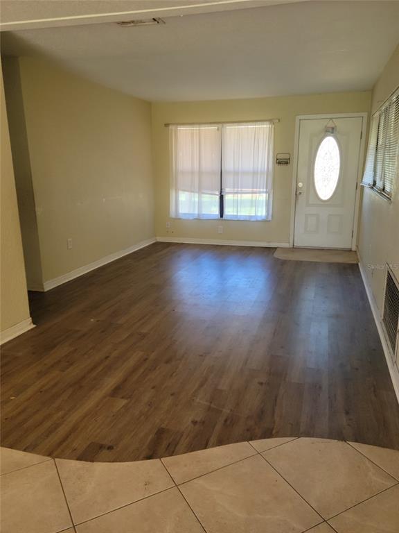 A living room features wood-look flooring, beige walls, a front door, and a large window — 1300 PARK AVENUE, TAVARES, FL