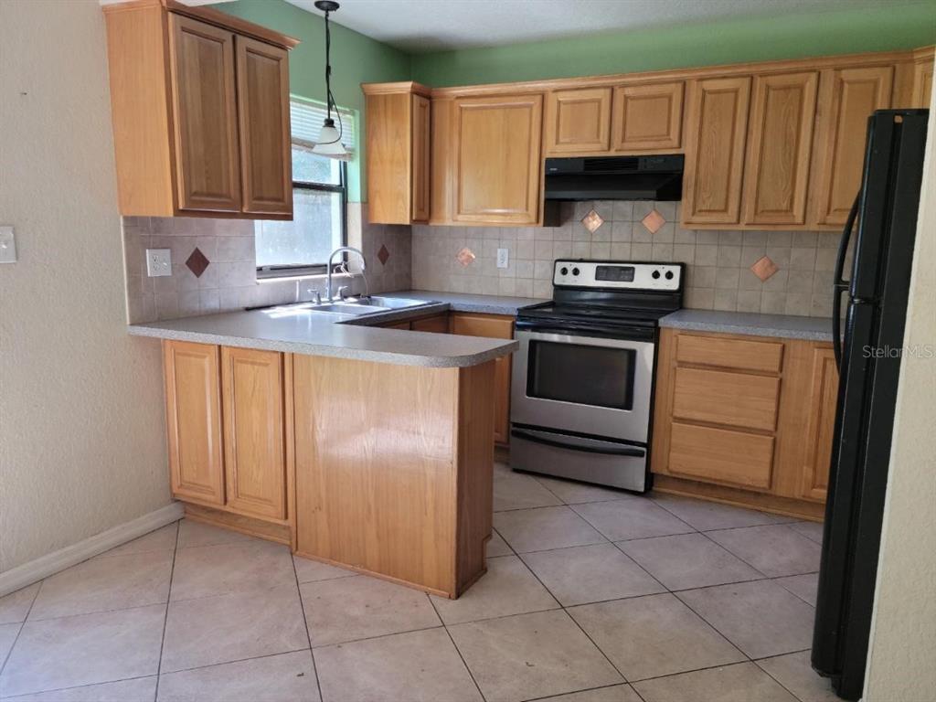 A kitchen with light wood cabinets, stainless steel appliances, and beige tile flooring — 1300 PARK AVENUE, TAVARES, FL