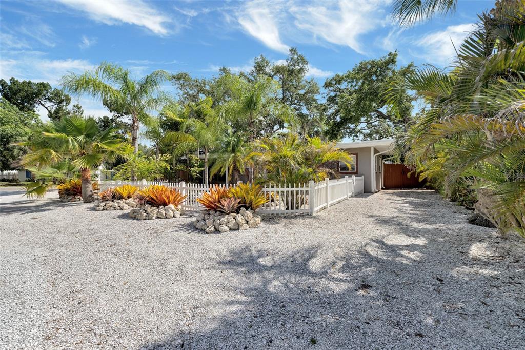 A gravel driveway leads to a house with a white picket fence and tropical landscaping — 1415 S SCHOOL AVENUE, SARASOTA, FL