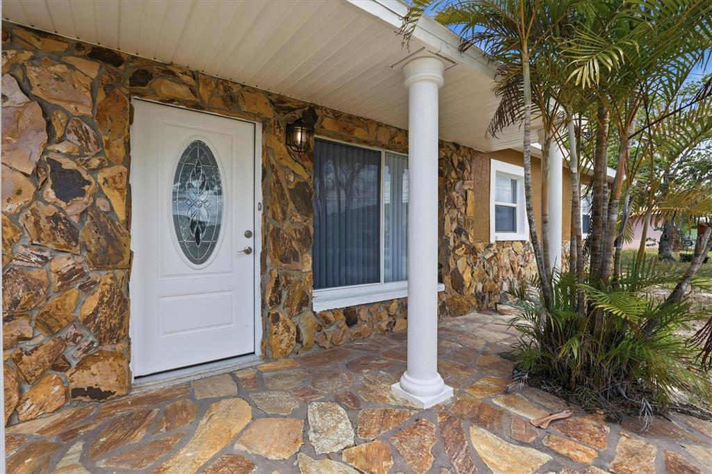 A white front door sits on a stone-covered porch with a white support column — 721 BAYSHORE DRIVE, TARPON SPRINGS, FL