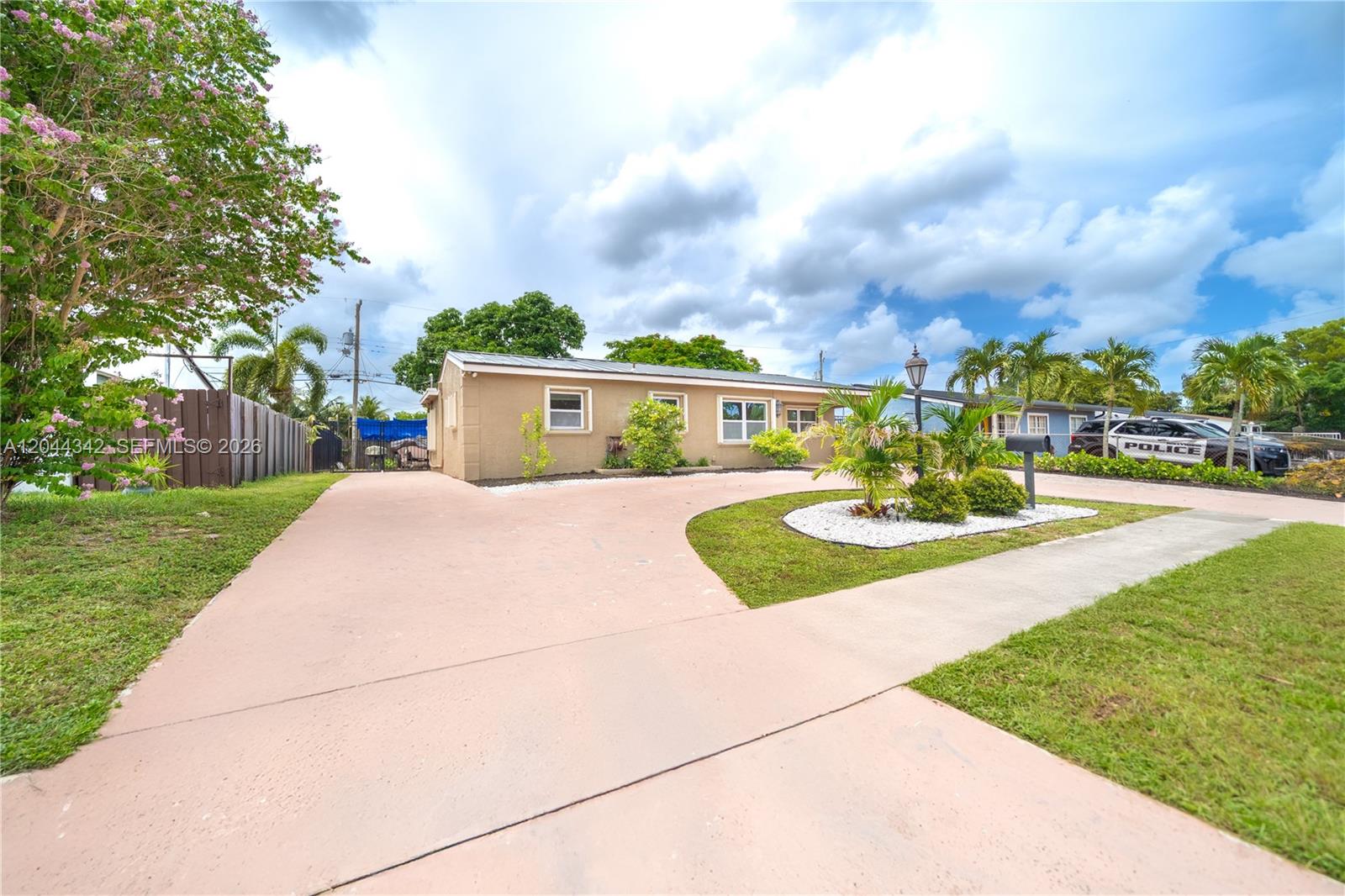 A single-story house with a tan exterior and a curved concrete driveway sits under clouds — 7101 Hope St, Hollywood FL 33024, HOLLYWOOD, FL