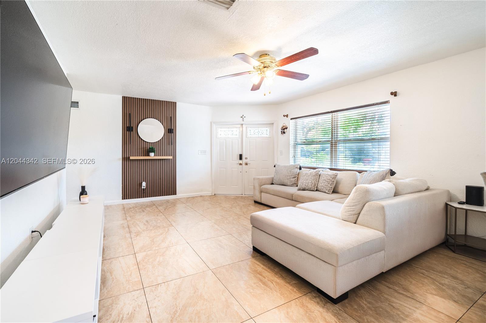A living room features a large sectional sofa, tile flooring, and a wood-slat accent wall — 7101 Hope St, Hollywood FL 33024, HOLLYWOOD, FL