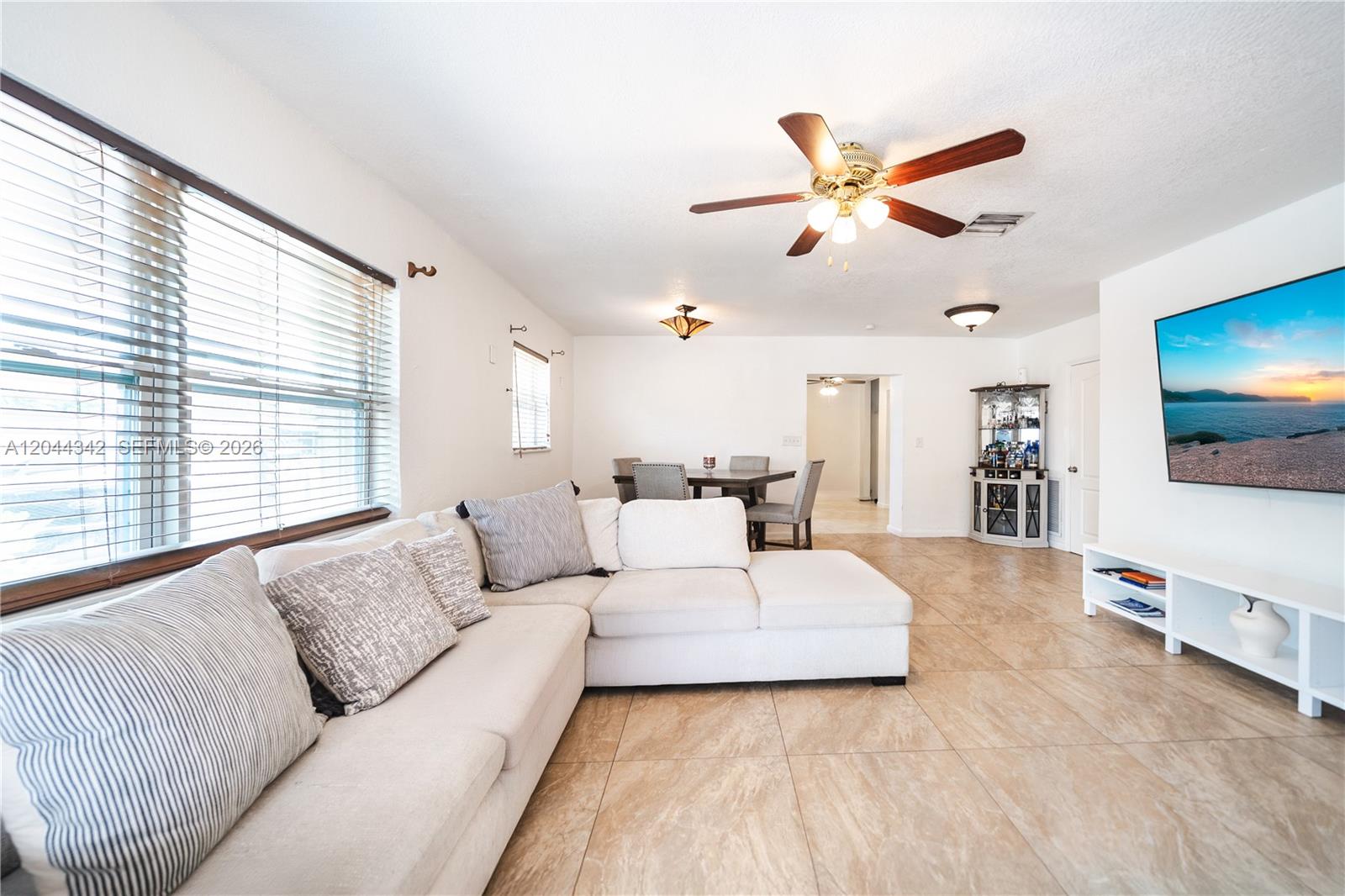 A living room features a white sectional sofa, tile flooring, and a wall-mounted television — 7101 Hope St, Hollywood FL 33024, HOLLYWOOD, FL