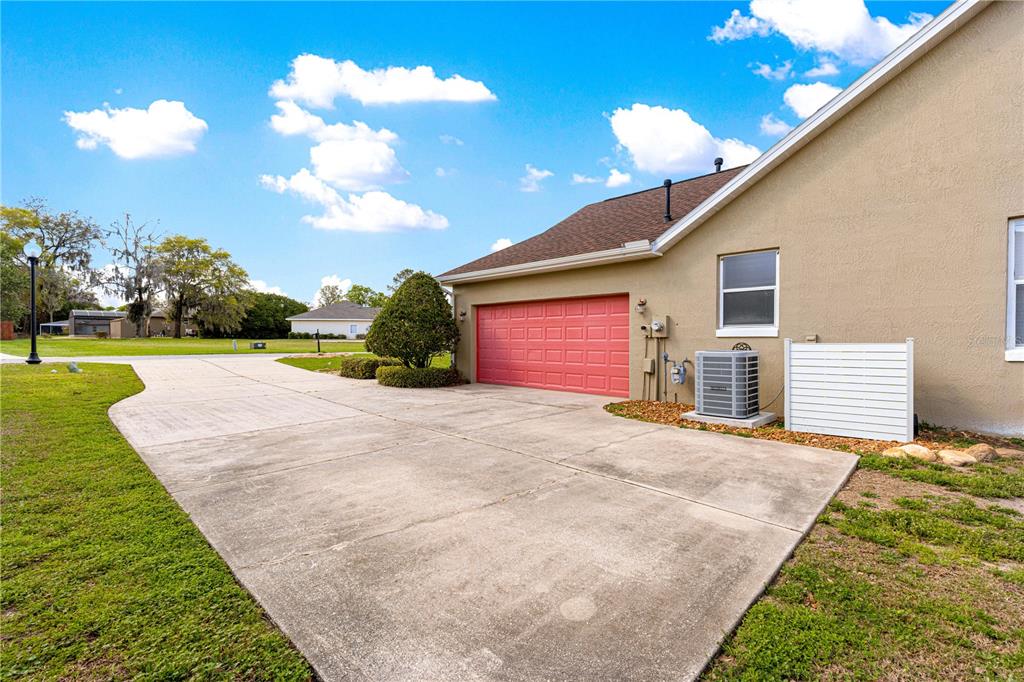 A concrete driveway leads to a house with a red garage door and exterior AC unit — 10485 SE 42ND COURT, BELLEVIEW, FL