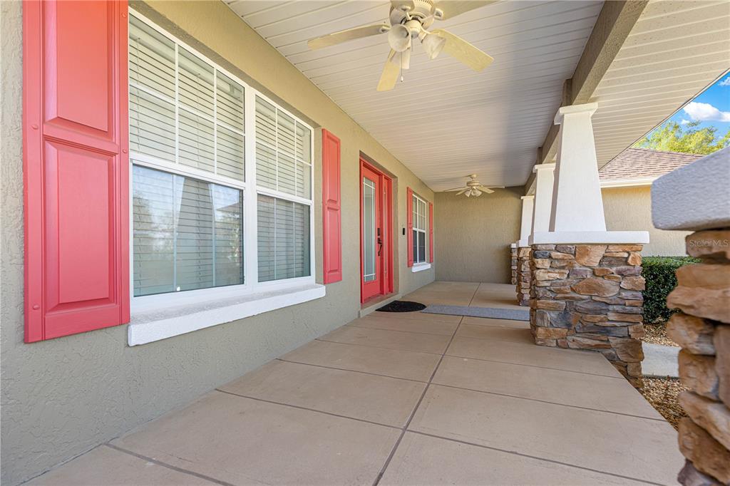 A covered front porch features a red door, red shutters, and stone-based columns — 10485 SE 42ND COURT, BELLEVIEW, FL
