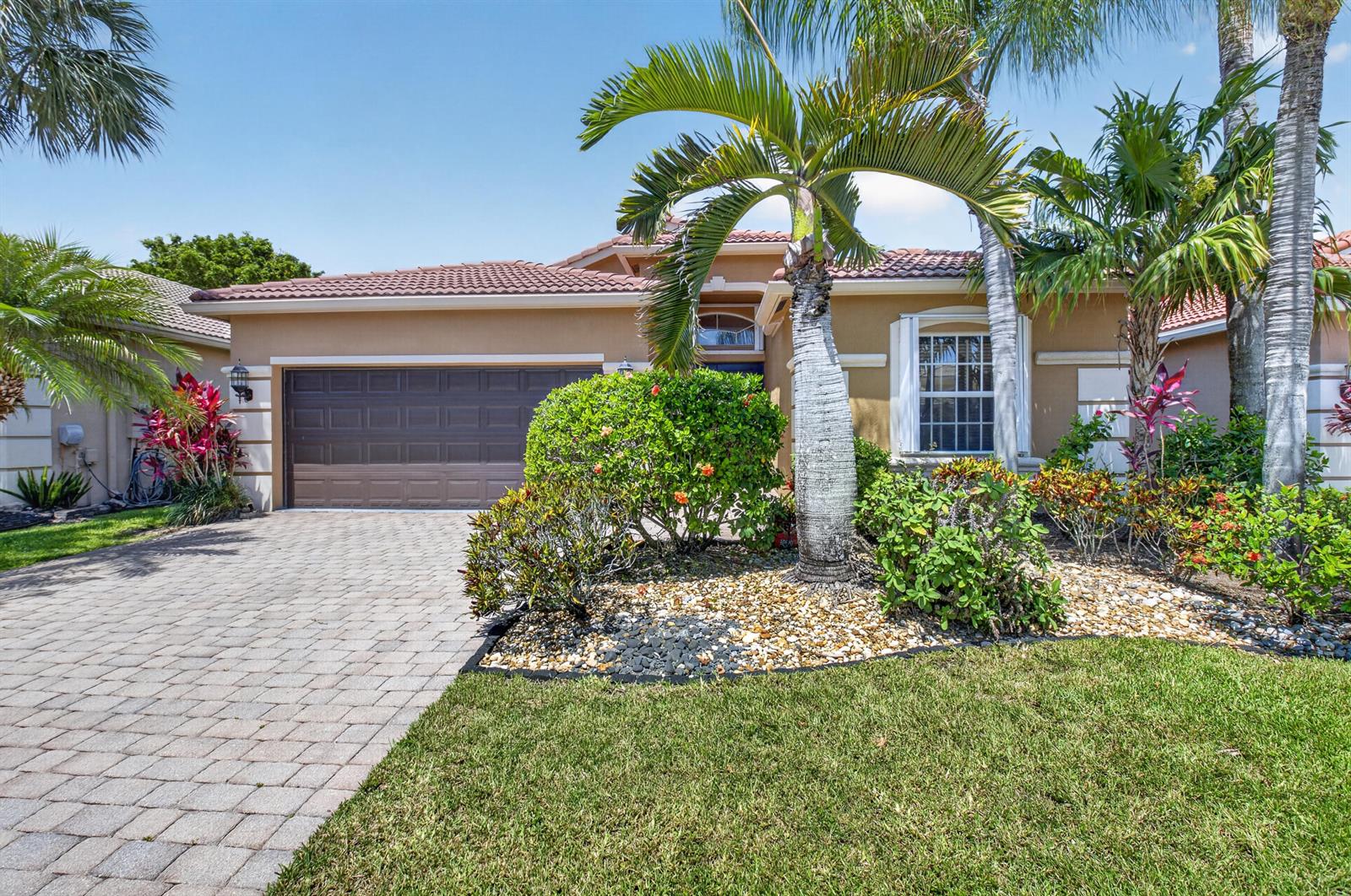 A single-story house with a paved driveway, a two-car garage, and tropical landscaping — 6761 Pisano Drive, Lake Worth FL 33467, LAKE WORTH, FL