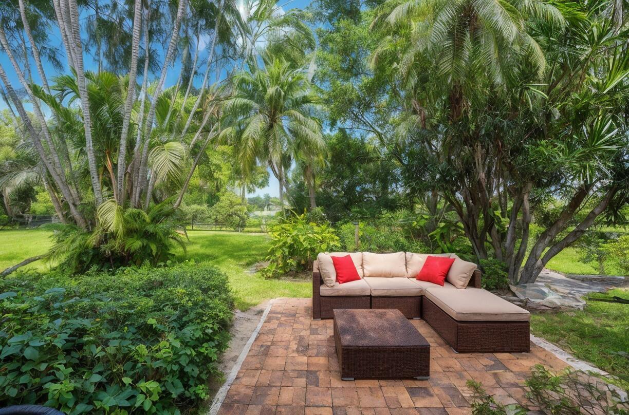 A patio with a wicker sectional sofa and coffee table sits in a lush backyard — 11397 Pond View Drive # E103, Wellington FL 33414, WELLINGTON, FL