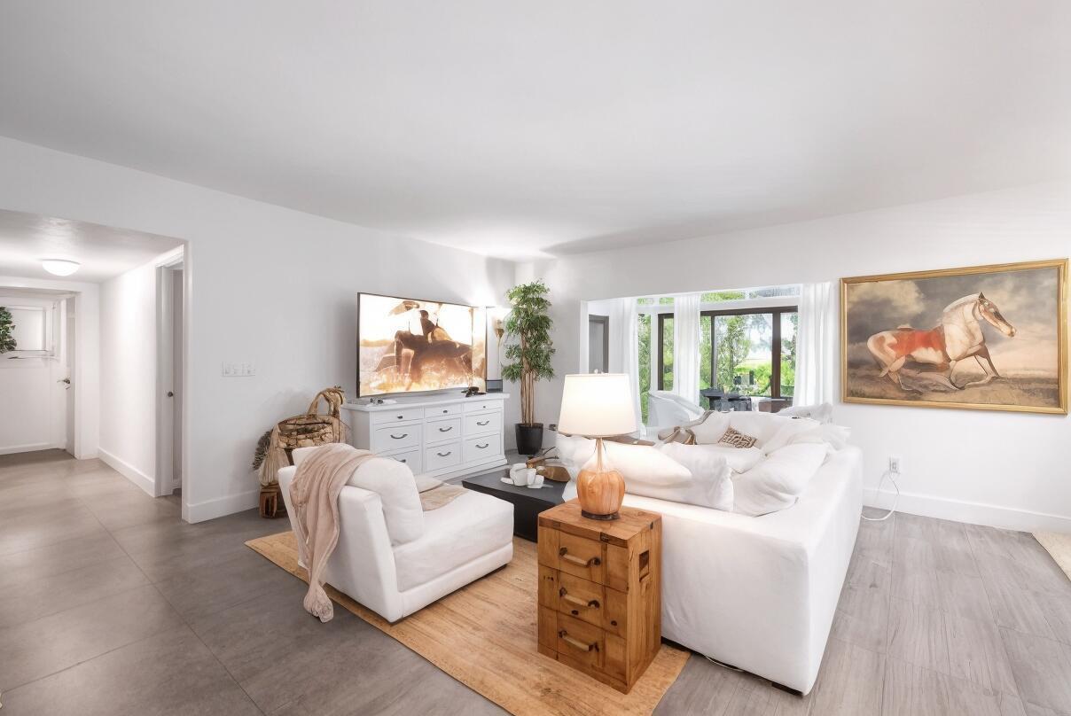 A bright living room features white furniture, a large horse painting, and gray tile flooring — 11397 Pond View Drive # E103, Wellington FL 33414, WELLINGTON, FL