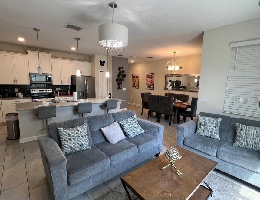 An open-concept living room and kitchen featuring gray sofas, a dining area, and white cabinetry — 420 OCEAN COURSE AVENUE, DAVENPORT, FL