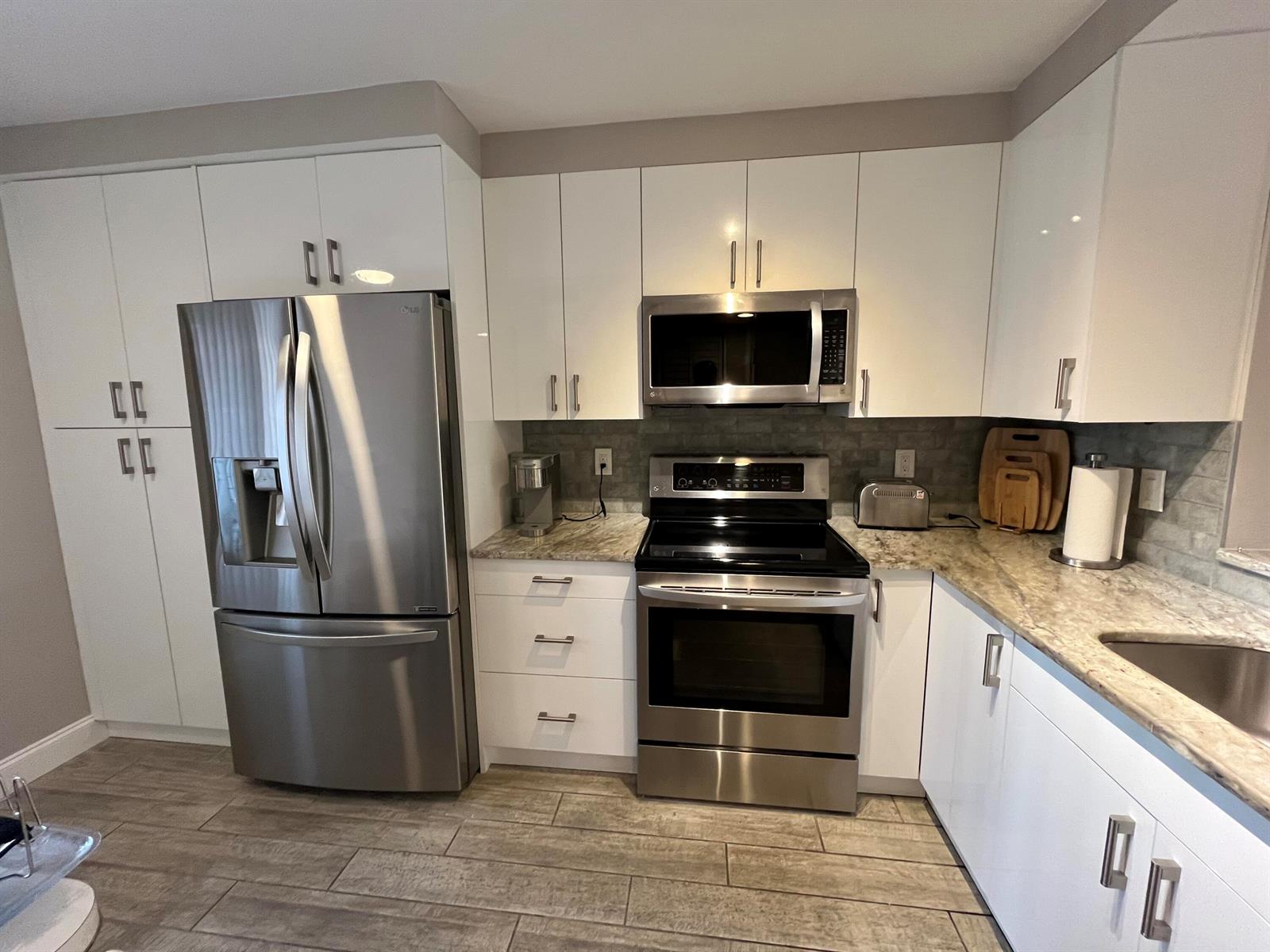 A modern kitchen features white cabinets, stainless steel appliances, and granite countertops — 7340 Amberly Lane # 205, Delray Beach FL 33446, DELRAY BEACH, FL