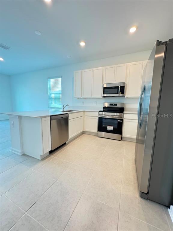 A modern kitchen features white cabinets, stainless steel appliances, and a central island with tile flooring — 6073 ZEN WAY, CLERMONT, FL