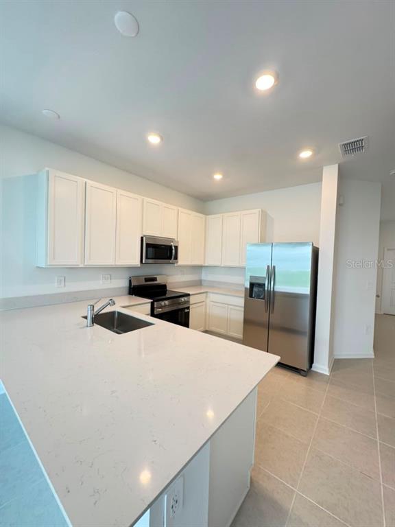 A modern kitchen features white cabinets, quartz countertops, stainless steel appliances, and tile flooring — 6073 ZEN WAY, CLERMONT, FL