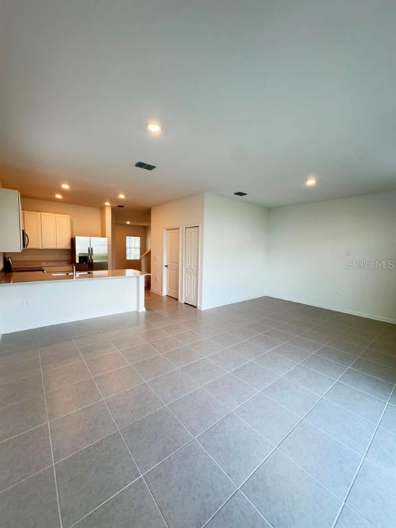 An open-concept kitchen with white cabinets and a breakfast bar overlooks a tiled living area — 6073 ZEN WAY, CLERMONT, FL