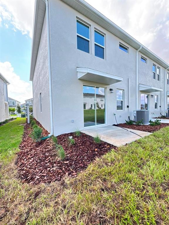 The exterior rear view of a two-story townhouse features a concrete patio and sliding doors — 6073 ZEN WAY, CLERMONT, FL