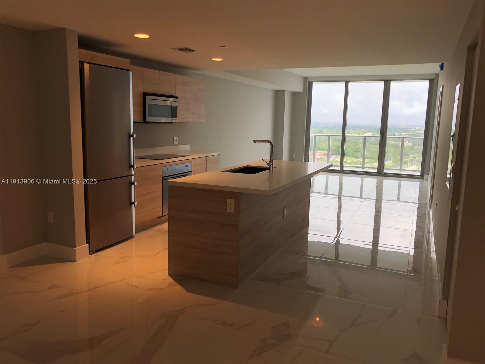 A modern kitchen features light wood cabinetry, stainless steel appliances, a central island, and floor-to-ceiling windows — 16385 Biscayne Blvd # 3003, North Miami Beach FL 33160, NORTH MIAMI BEACH, FL