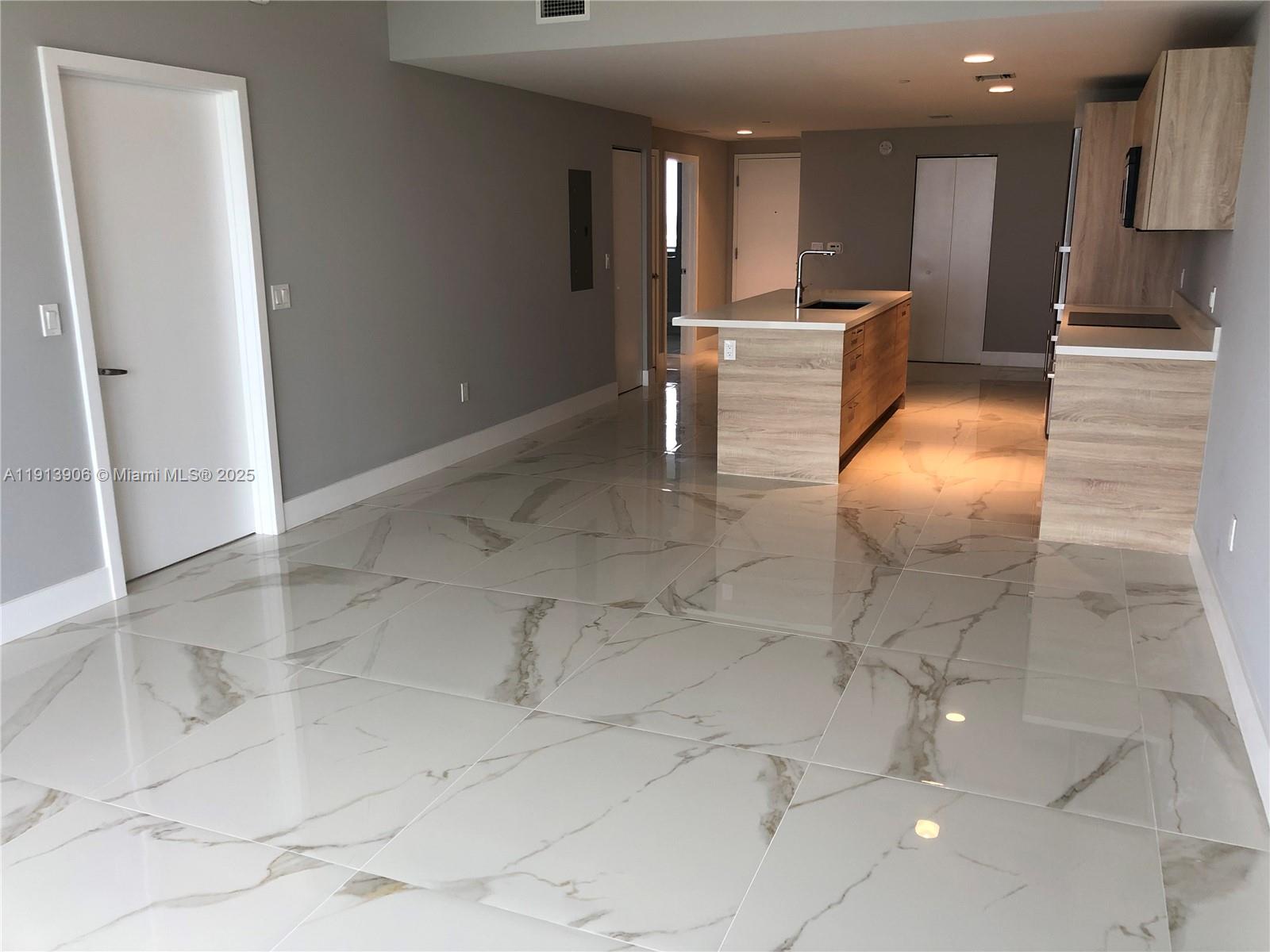 A modern kitchen features light wood cabinetry, a central island, and polished marble-look tile flooring — 16385 Biscayne Blvd # 3003, North Miami Beach FL 33160, NORTH MIAMI BEACH, FL
