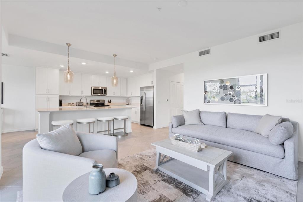 An open-concept living room and kitchen featuring white cabinetry, stainless steel appliances, and gray furniture — 14161 HERITAGE LANDING BOULEVARD UNIT 1112, PUNTA GORDA, FL