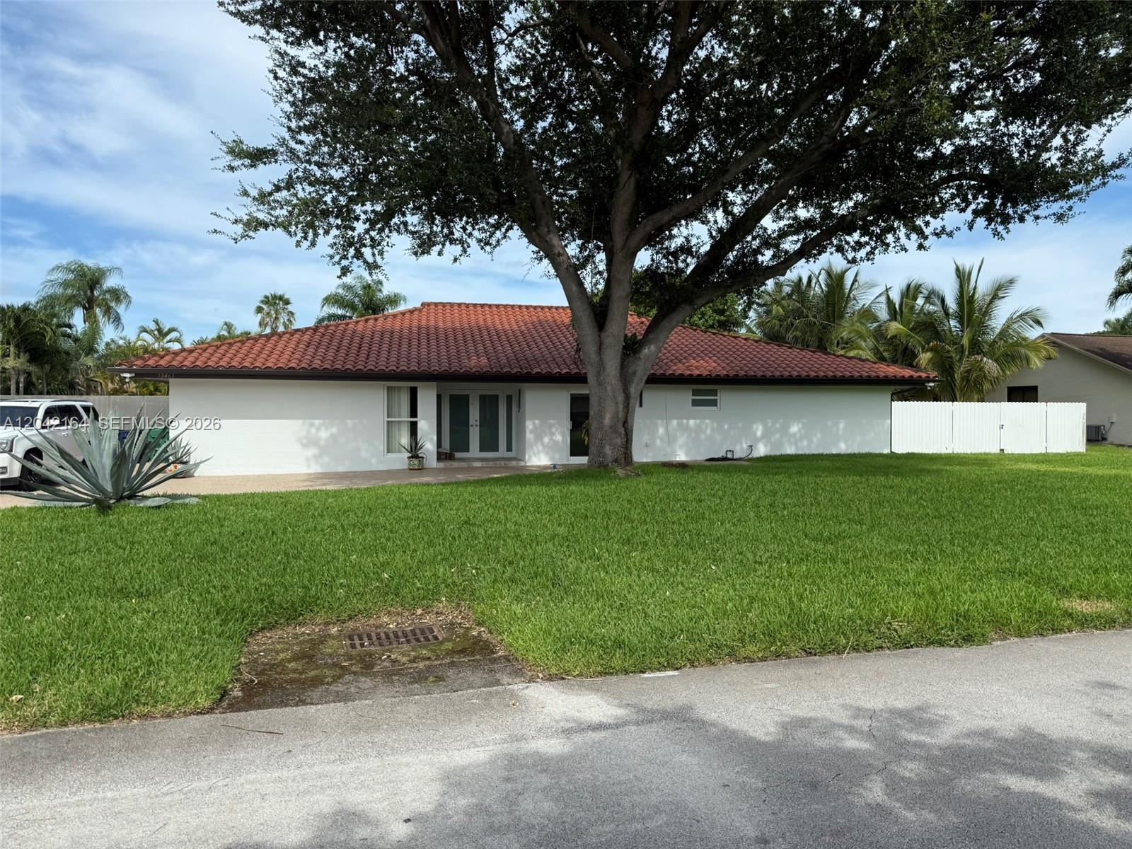 A single-story white house with a red tile roof stands behind a large tree — 13461 SW 98th Pl # 13461, Miami FL 33176, MIAMI, FL