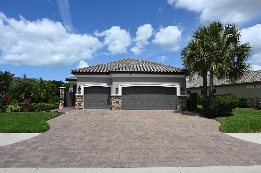 A single-story house with a paver driveway, stone accents, and a three-car garage — 9760 HIGHLAND PARK PLACE, PALMETTO, FL