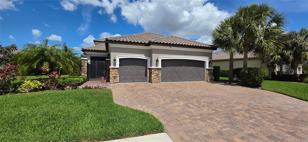 A tan stucco house with a tiled roof, stone accents, and a landscaped front yard — 9760 HIGHLAND PARK PLACE, PALMETTO, FL
