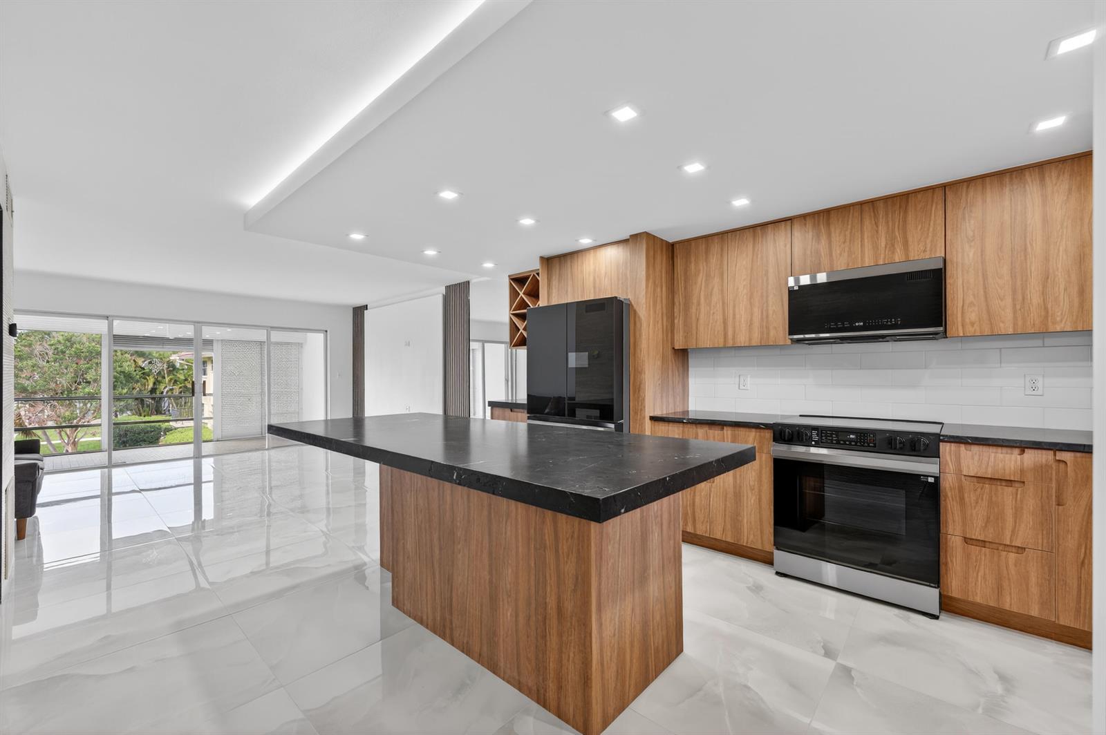 A modern kitchen features wood cabinets, a black island, and white tile floors — 2134 NE 36th Street # 82, Lighthouse Point FL 33064, LIGHTHOUSE POINT, FL