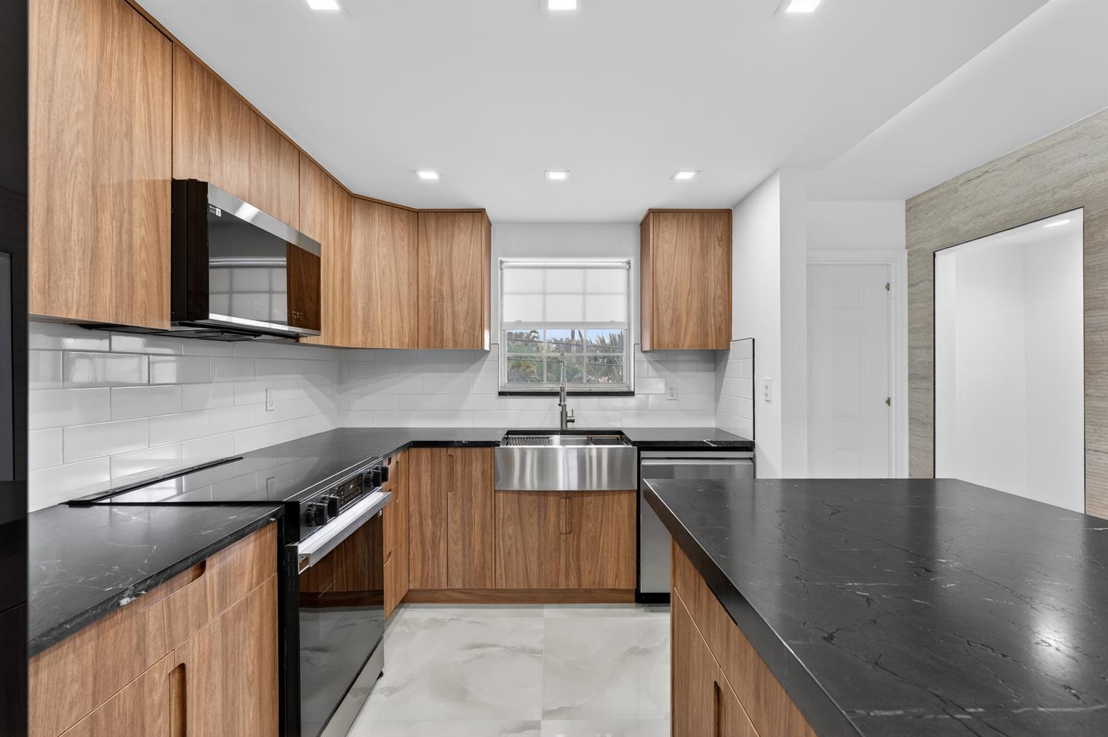 A modern kitchen features wood cabinets, black countertops, a farmhouse sink, and white tile backsplash — 2134 NE 36th Street # 82, Lighthouse Point FL 33064, LIGHTHOUSE POINT, FL