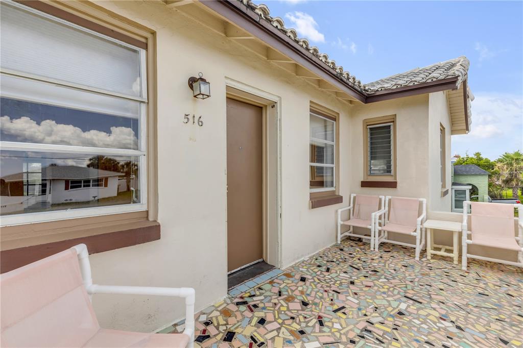 A patio with a mosaic tile floor features several chairs and a tan exterior wall — 516 WISTERIA ROAD, DAYTONA BEACH, FL