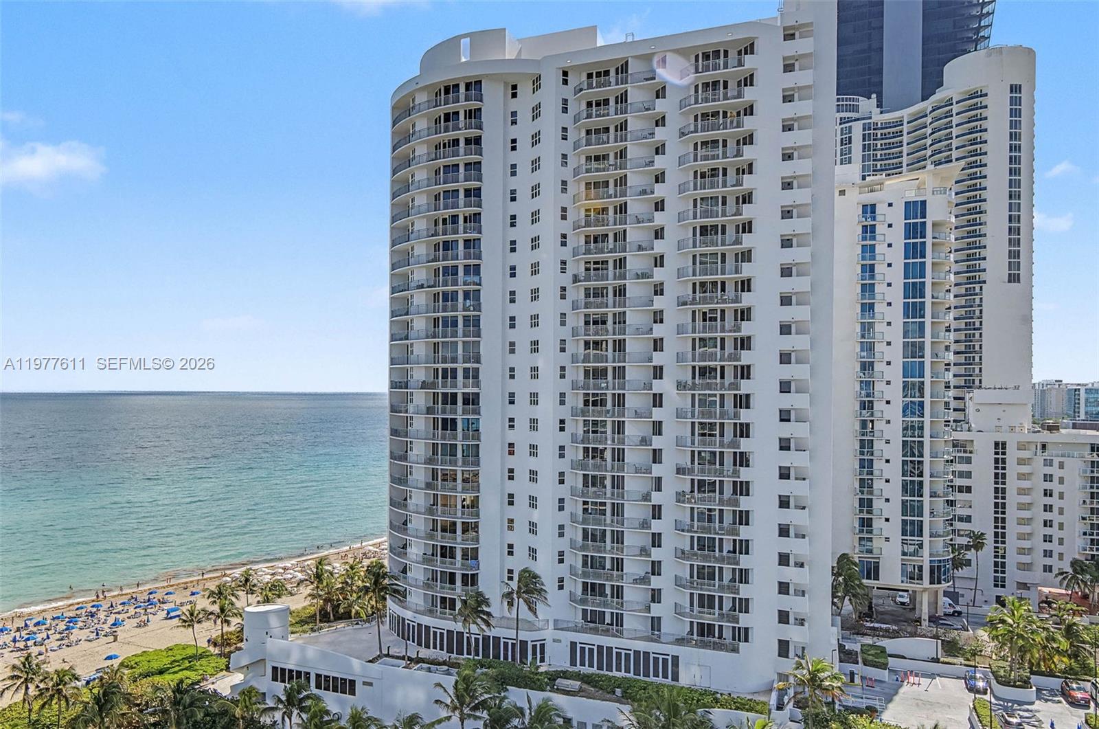 A tall white residential high-rise building stands next to a sandy beach and ocean — 17475 Collins Ave # 904, Miami Beach FL 33160, MIAMI BEACH, FL
