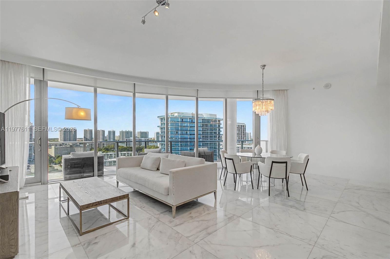 A bright living and dining area features white marble floors, floor-to-ceiling windows, and city views — 17475 Collins Ave # 904, Miami Beach FL 33160, MIAMI BEACH, FL
