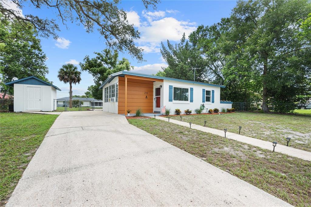 A single-story house with a white exterior, blue shutters, and a wood-paneled porch entrance — 215 ABBEYVILLE STREET, DELTONA, FL