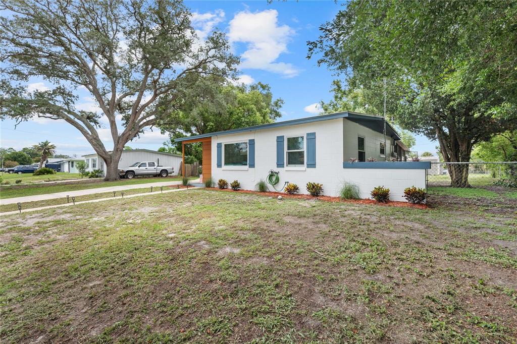 A single-story white house with blue shutters sits on a grassy lot with large trees — 215 ABBEYVILLE STREET, DELTONA, FL