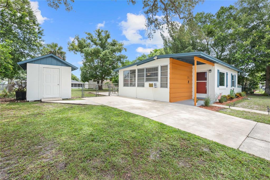 A single-story house with a white exterior, orange accent wall, and a detached storage shed — 215 ABBEYVILLE STREET, DELTONA, FL